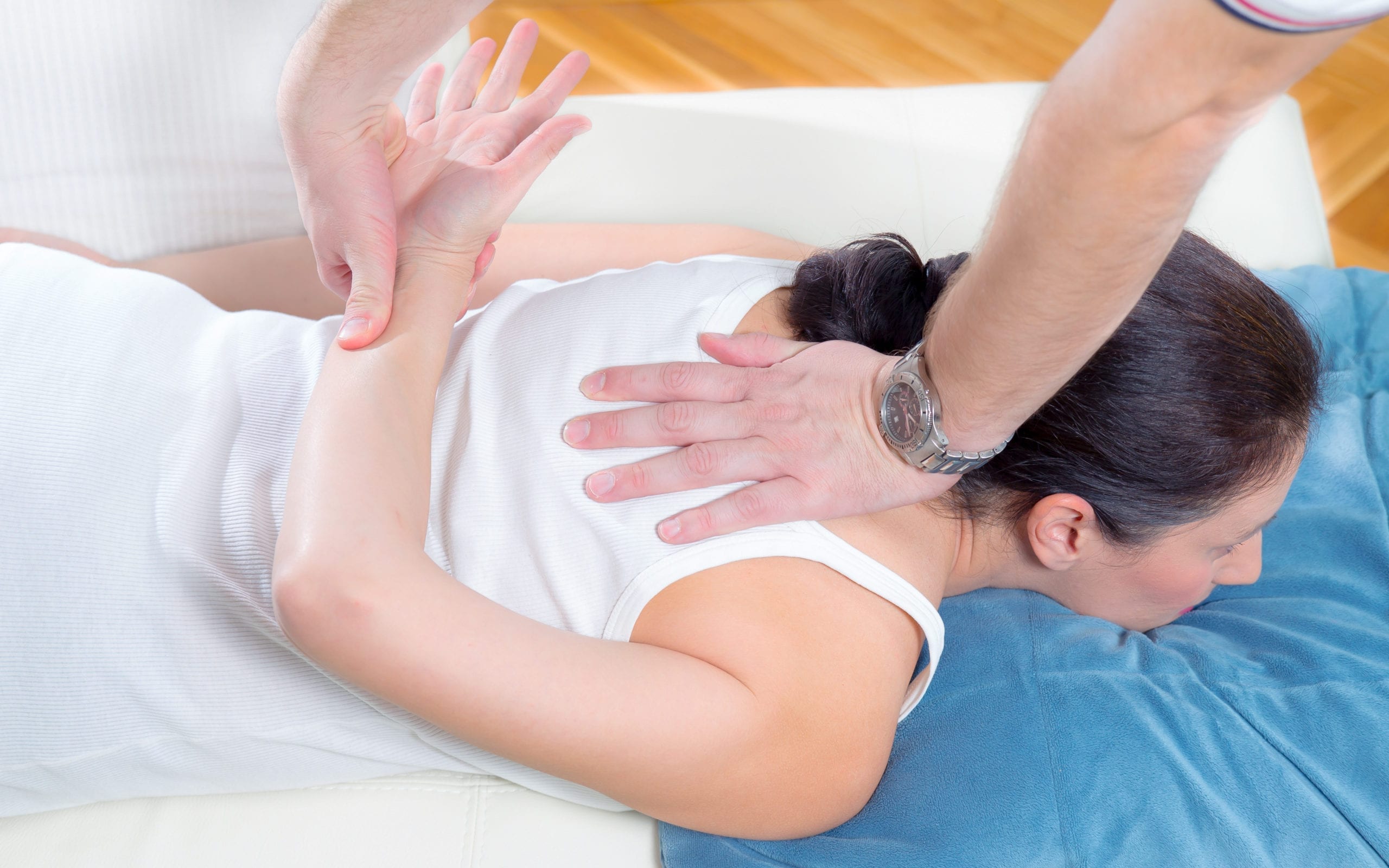 A therapists hands manipulating a patients back and arm